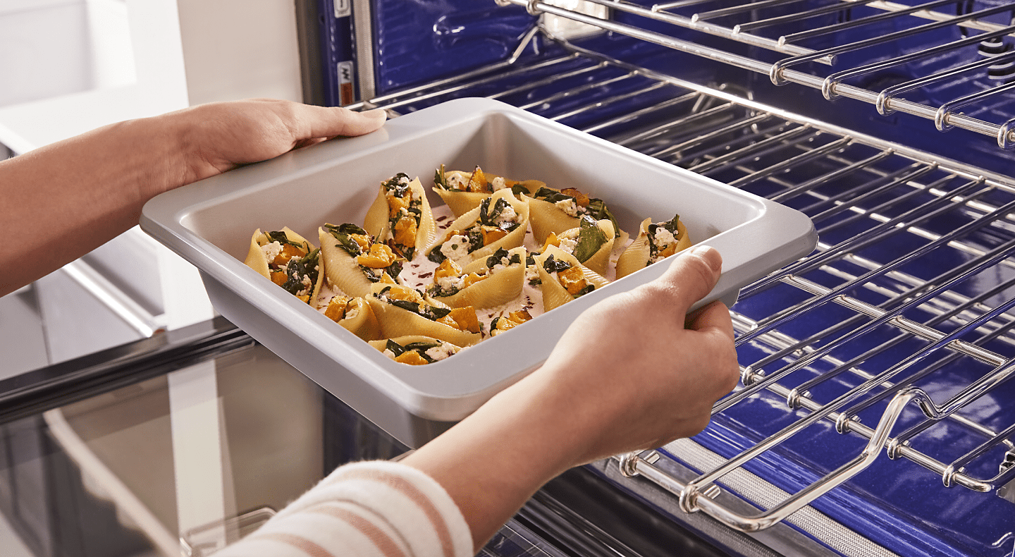 A person placing a tray of stuffed shells on the lower rack of a convection oven