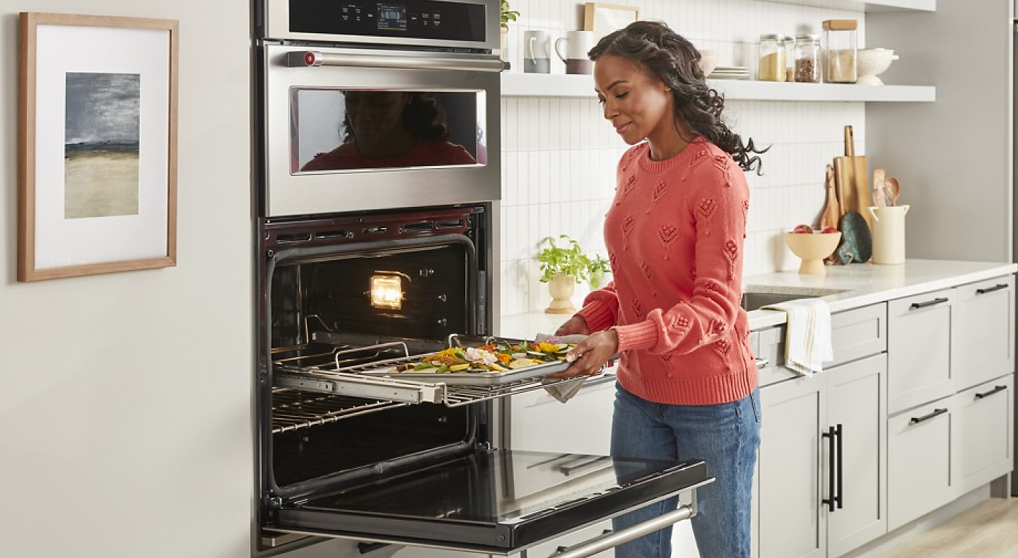 A woman using a KitchenAid® combination oven to roast vegetables