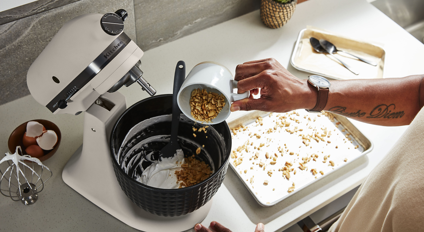 Man pouring nuts into the bowl of a KitchenAid® stand mixer