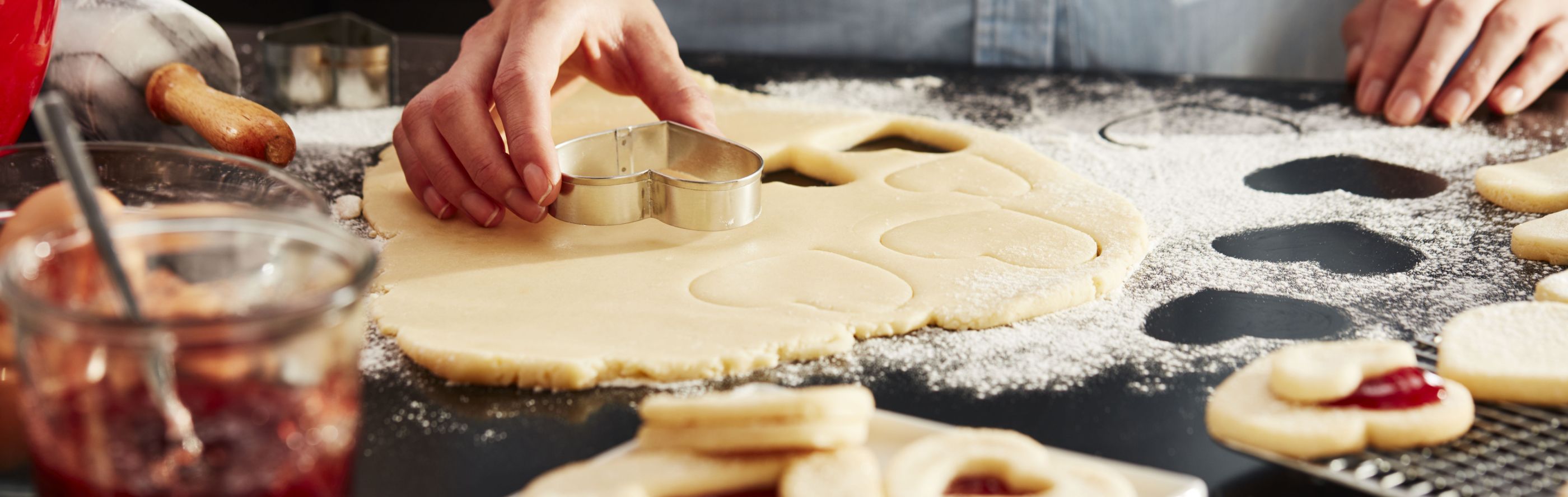Woman cutting out cookies with a heart-shaped cookie cutter.