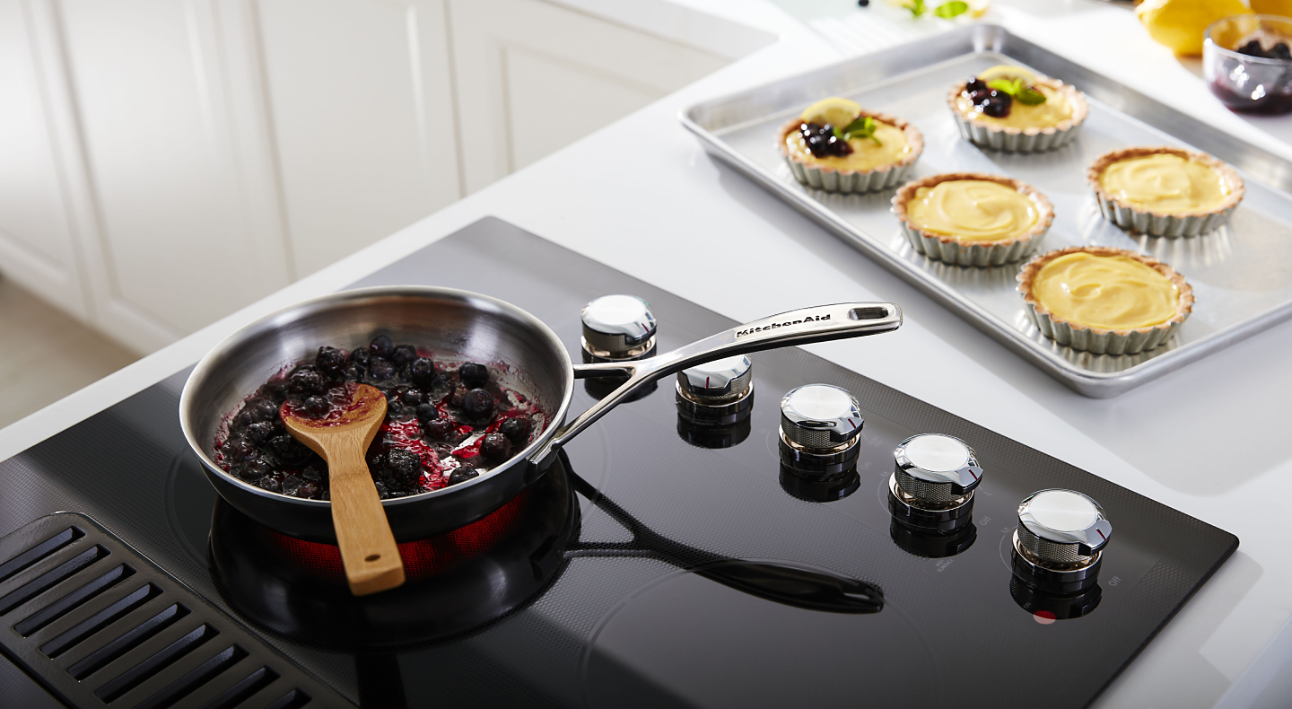Cooked fruit on a black cooktop next to a pan of baked desserts 