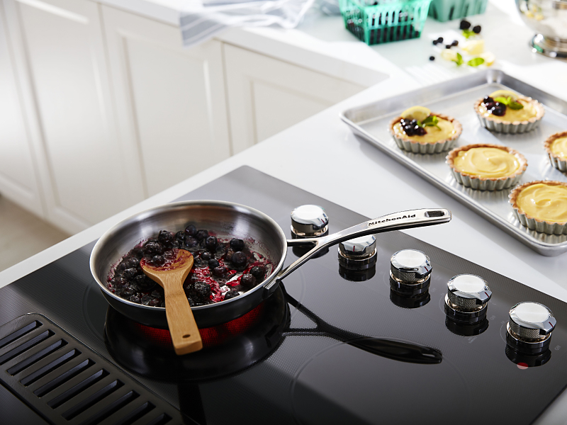 Cooked fruit on a black cooktop next to a pan of baked desserts 