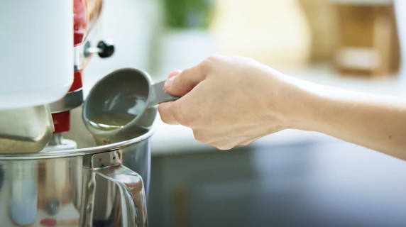 A person pouring oil into a KitchenAid® stand mixer bowl.