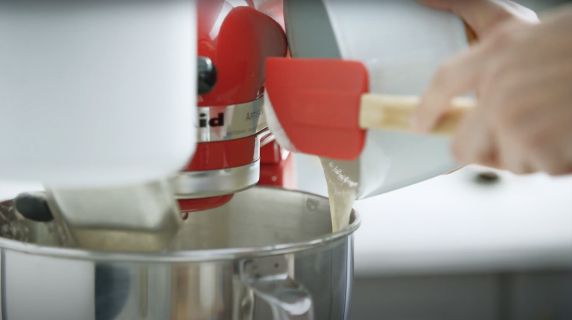 A person adding sourdough starter to a KitchenAid® stand mixer bowl.