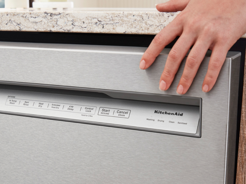 Hand touching a stainless steel KitchenAid® front control dishwasher