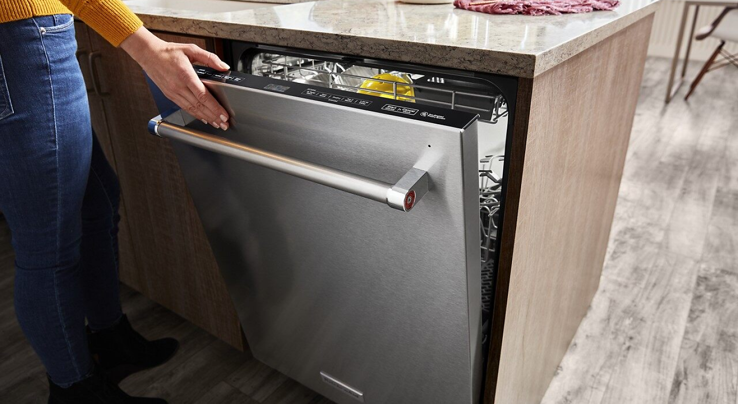 A closeup of a person’s hand closing a stainless steel KitchenAid® dishwasher.