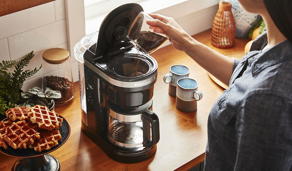 Woman pouring grounds into auto drip coffee maker