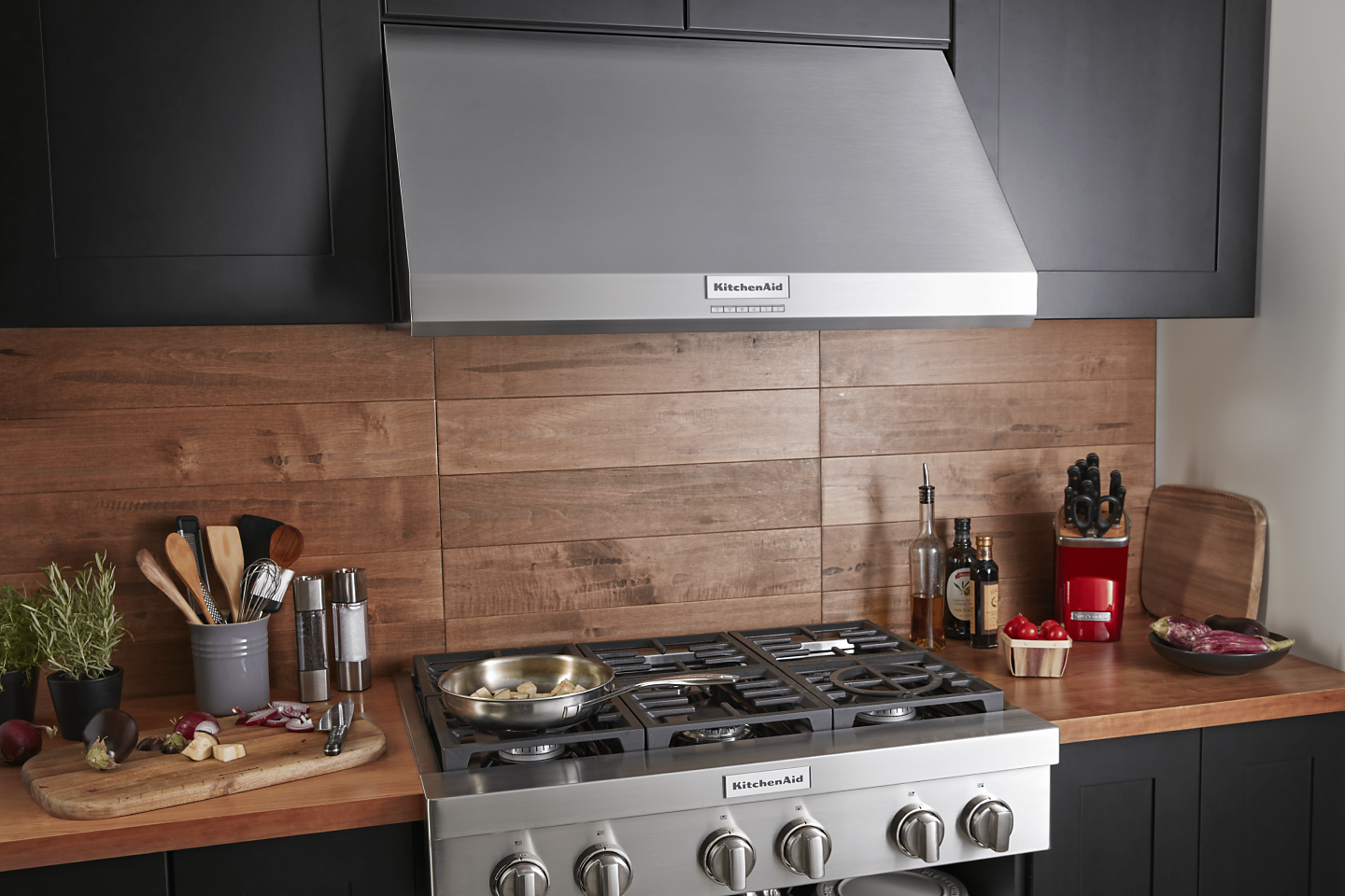 A full kitchen space with cabinets, an oven and a KitchenAid® range hood 