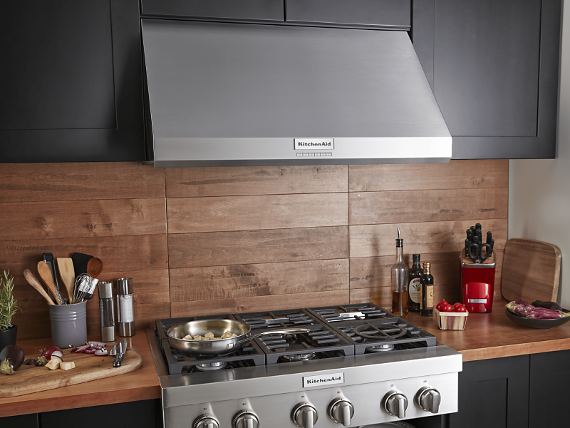 A full kitchen space with cabinets, an oven and a KitchenAid® range hood 