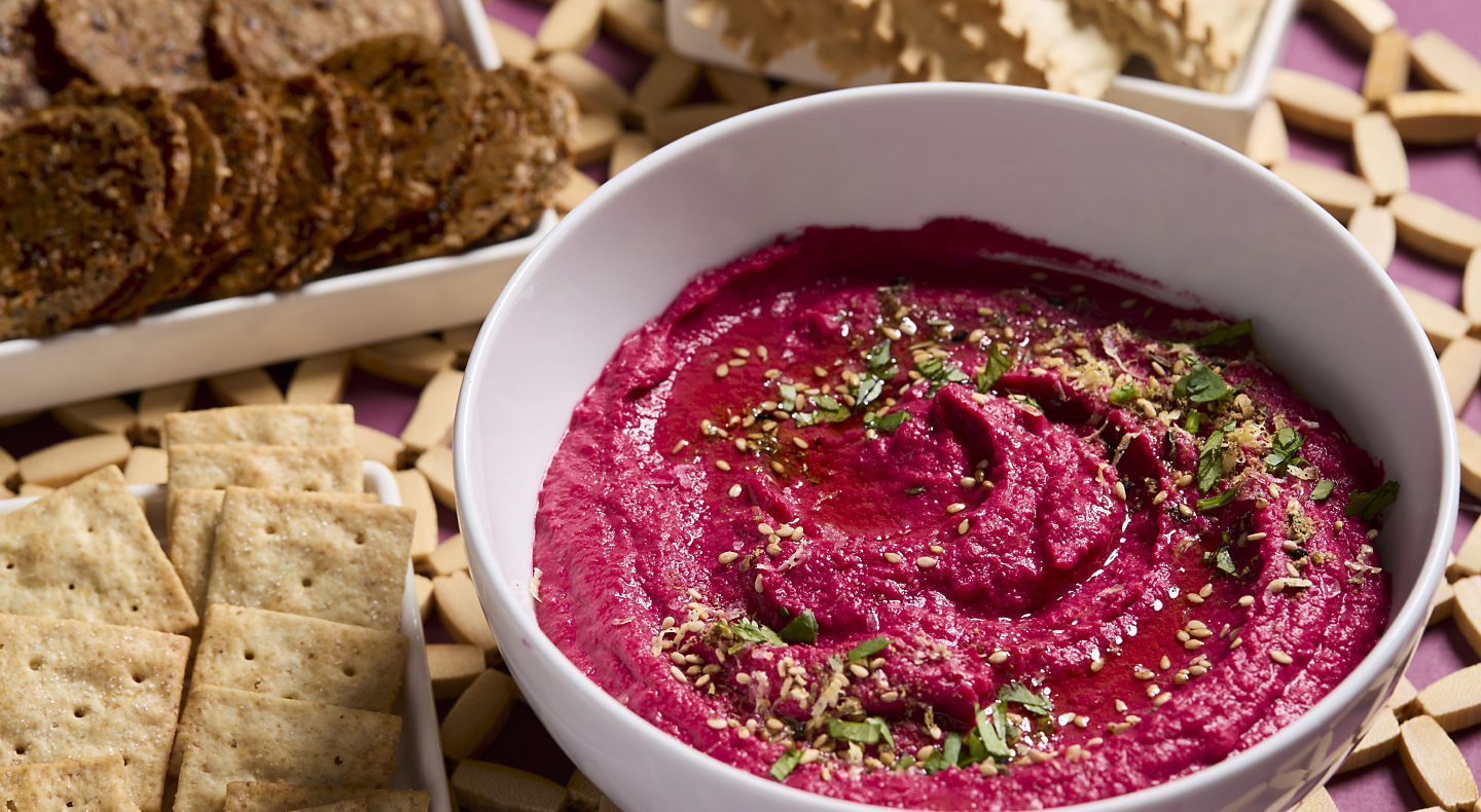 Beet hummus topped with herbs in a white bowl