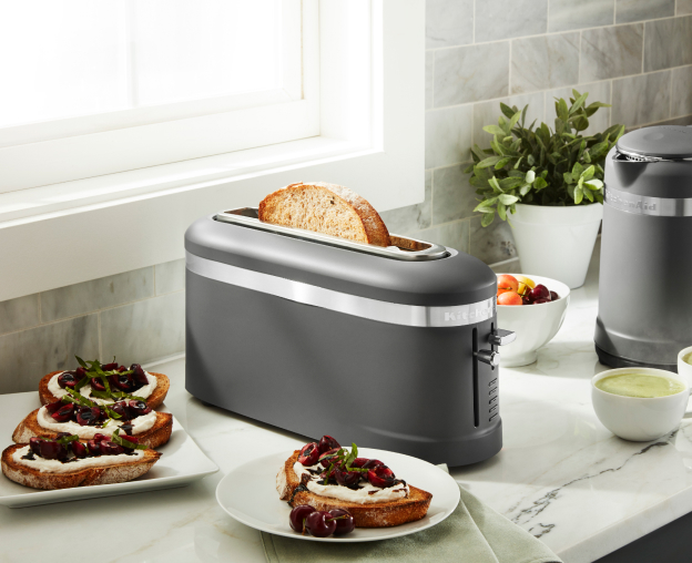 Toaster on a kitchen counter next to toast with fruit preserves 
