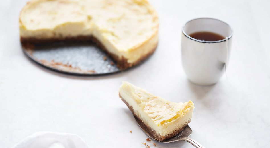 A piece of custard crumb pie on a pie server next to a cup of tea and the rest of the pie.