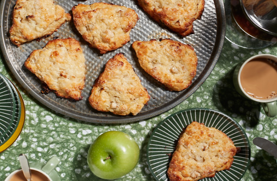 Baked scones in a pan next to an apple and a cup of coffee