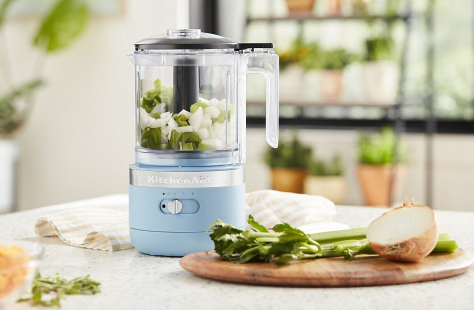 Blue food chopper with chopped celery and onions in bright kitchen
