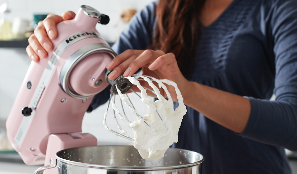 Woman holding a pink KitchenAid brand stand mixer with frosting on whisk