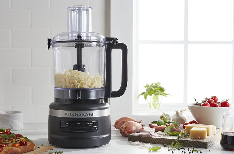 Black KitchenAid brand food processor with shredded cheese next to cutting board and flatbread
