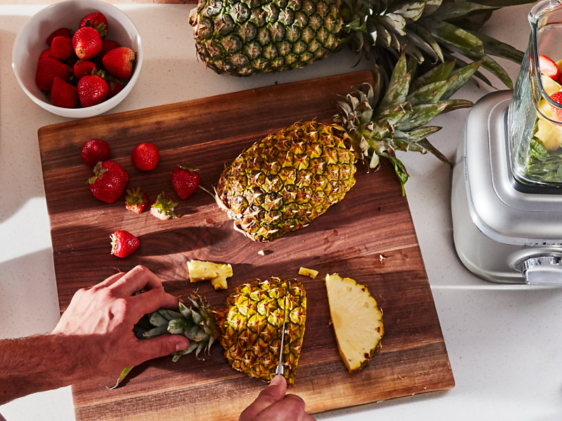 Person cutting pineapple next to a KitchenAid® blender