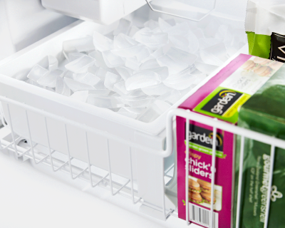 Full ice maker bin inside of a freezer next to frozen goods