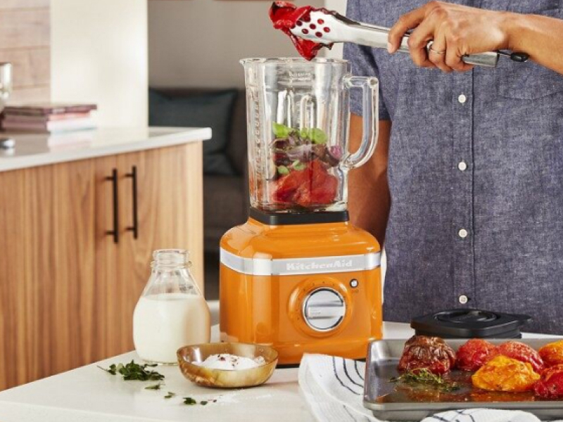 Person adding ingredients to orange KitchenAid® countertop blender