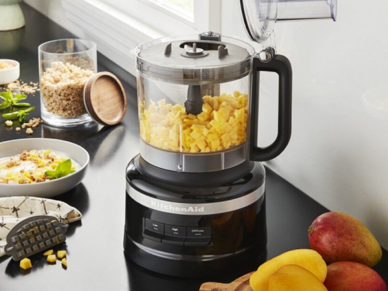 Black KitchenAid® food processor filled with corn kernels on counter with ingredients