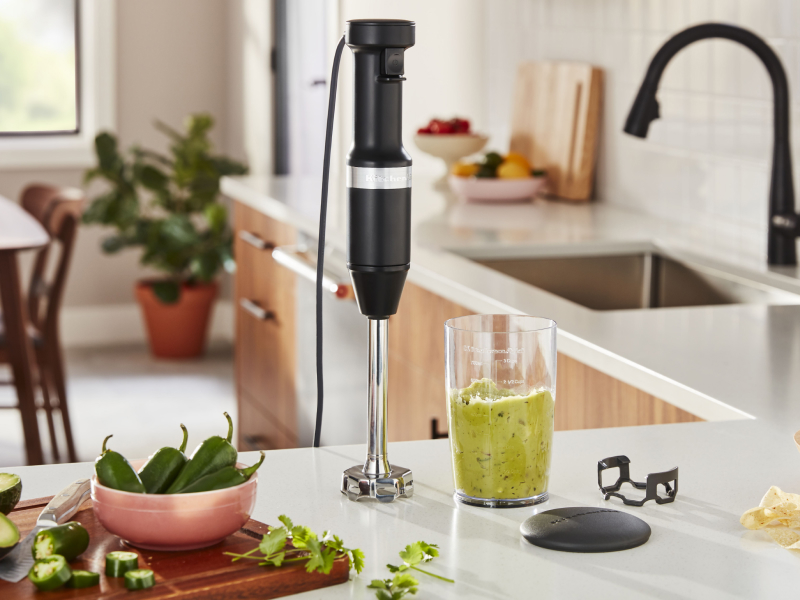 Black KitchenAid® hand blender on counter with blending cup and ingredients