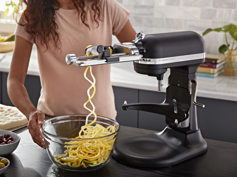 Matte black KitchenAid® stand mixer spiralizing food with the Spiralizer with Peel, Core and Slice Attachment