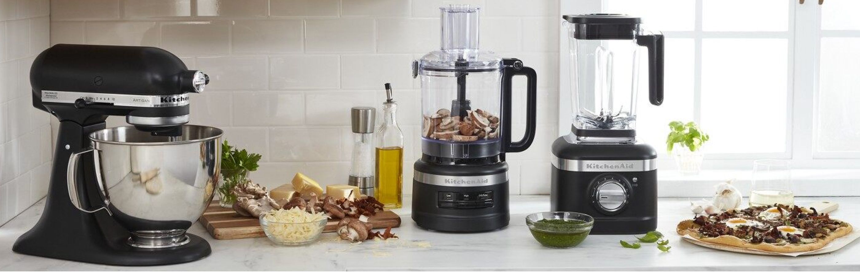 Black KitchenAid® stand mixer, food processor and blender on countertop with ingredients