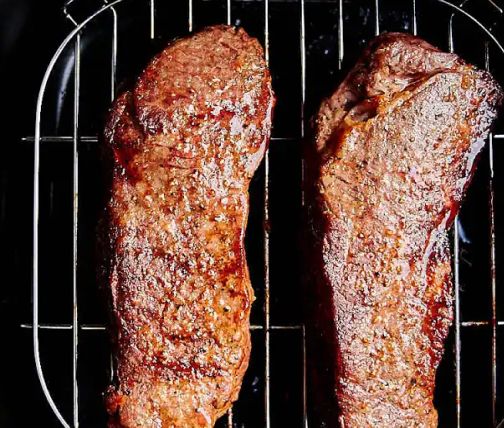 Two steak strips cooked on an air fryer basket
