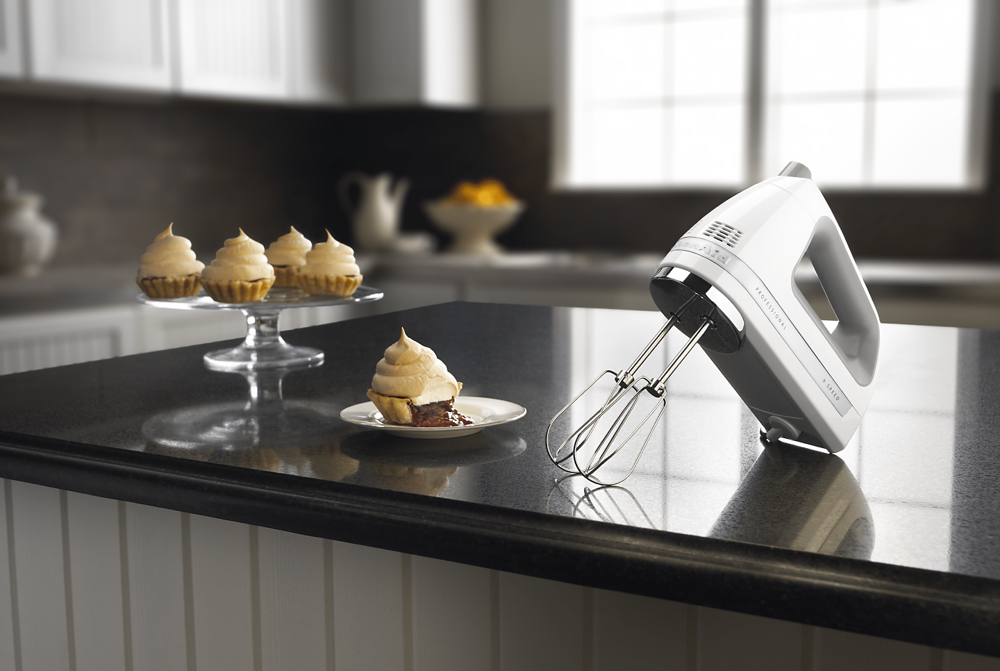 Stainless steel KitchenAid® hand mixer on countertop with cream-topped mini pie desserts