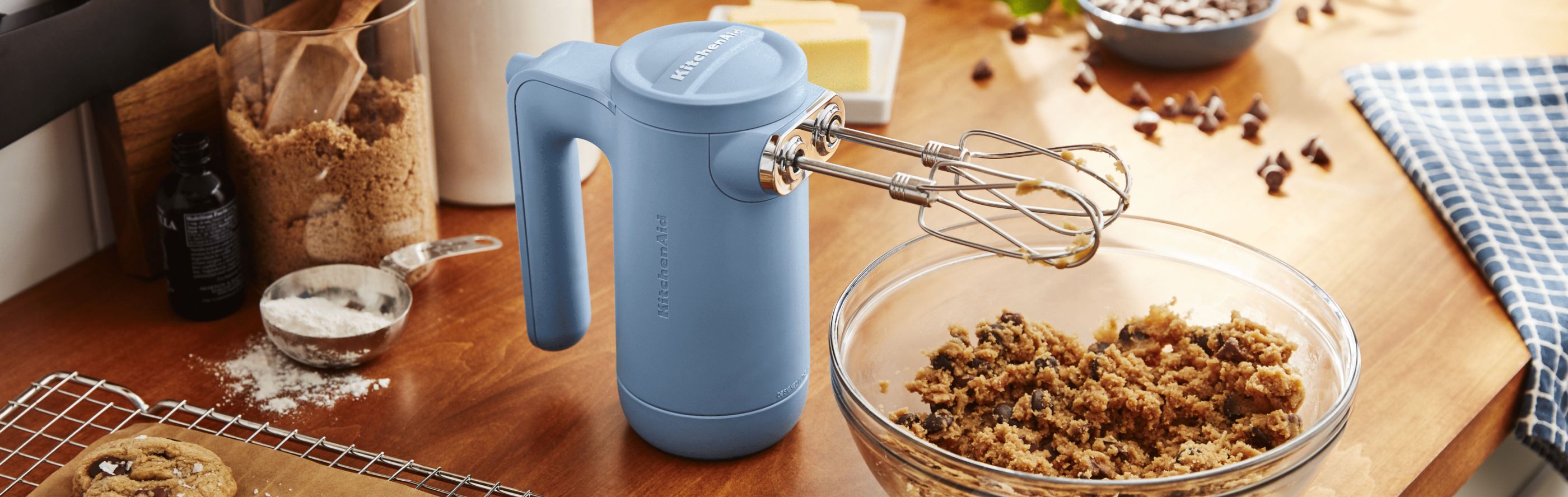 Blue KitchenAid® hand mixer on countertop next to bowl of chocolate chip cookie dough