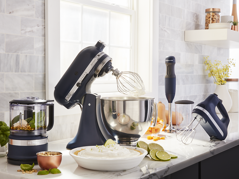 Black KitchenAid® food processor, stand mixer, hand mixer and immersion blender on countertop with key lime pie and ingredients