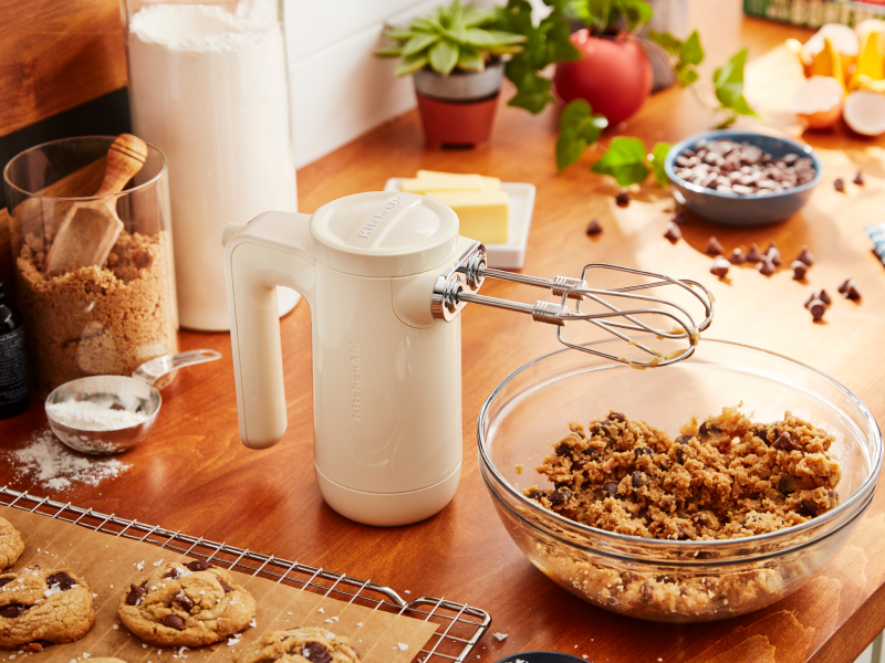 White KitchenAid® hand mixer resting on countertop above bowl of cookie dough