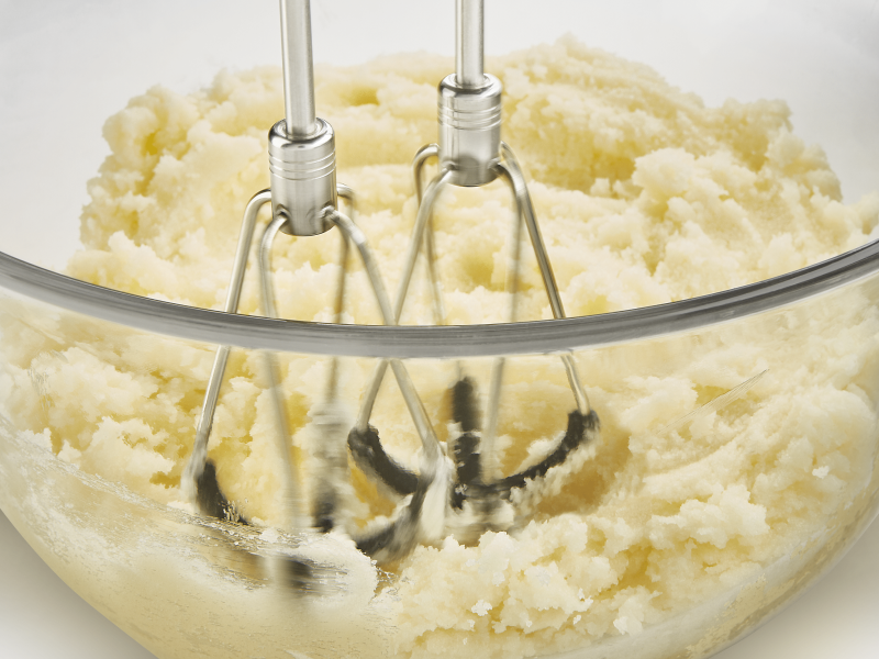 Close up of flex edge beaters mixing mashed potatoes in glass bowl