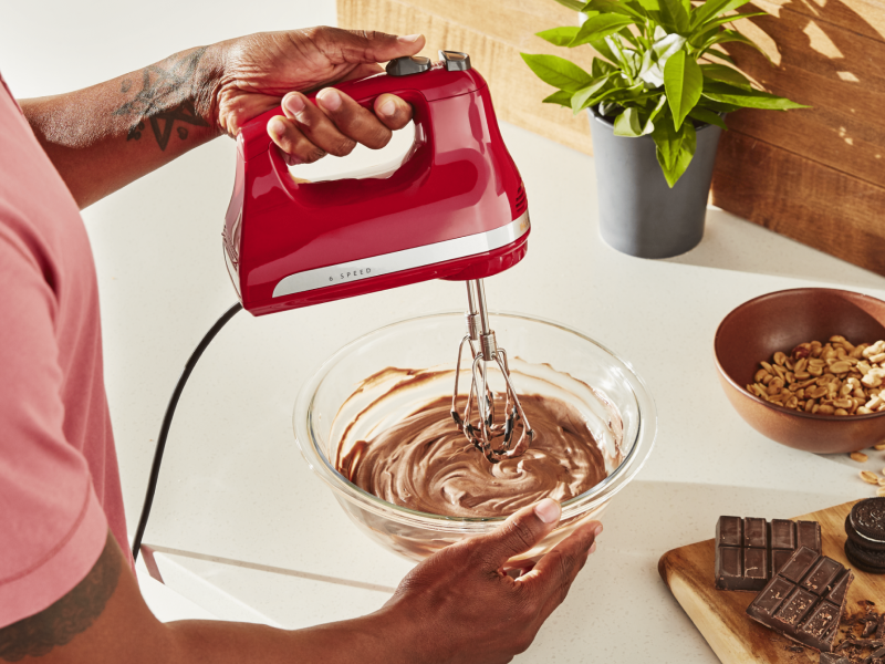 Maker using red KitchenAid® hand mixer to blend chocolate mousse in glass bowl