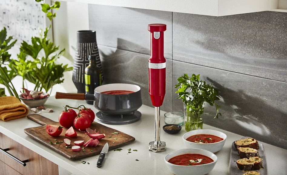 Red KitchenAid® Cordless Variable Speed Hand Blender with bowls of tomato soup