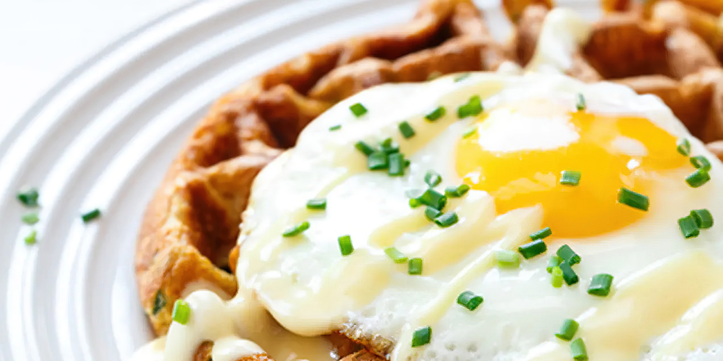A waffle sitting on a plate, topped with a fried egg and chives.