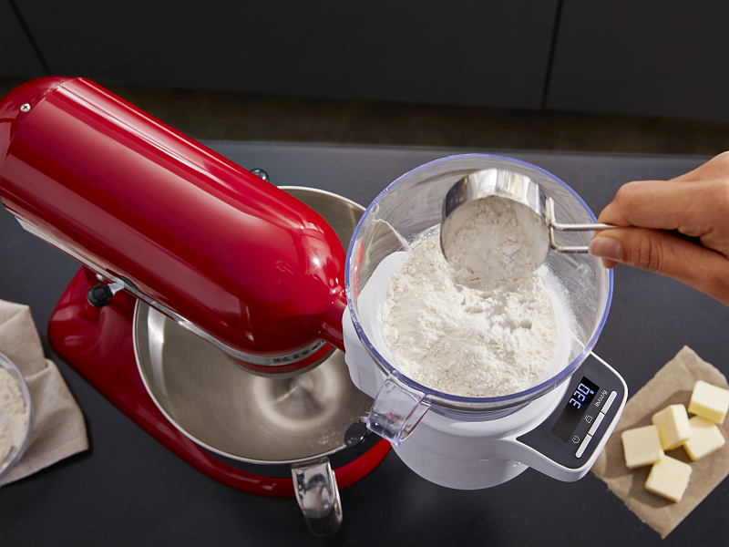 A person sifting flour into a red KitchenAid® stand mixer.