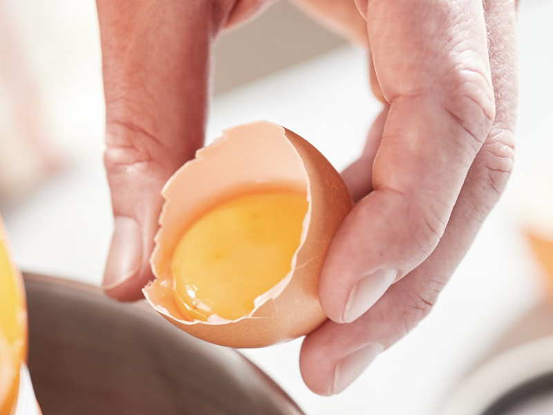 A person holding a cracked egg shell with yolk inside