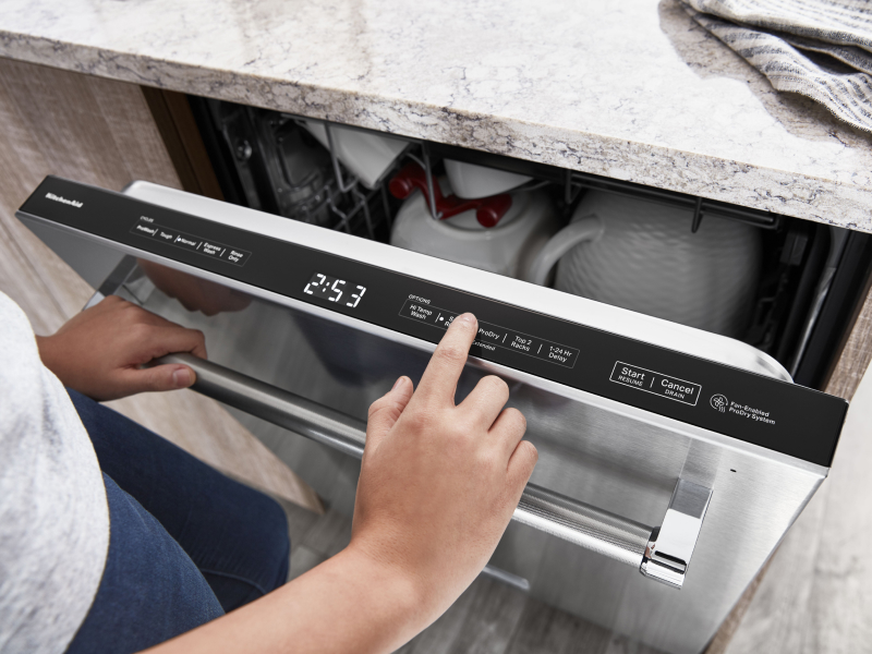 A closeup of a person using the control pad of a KitchenAid® dishwasher.