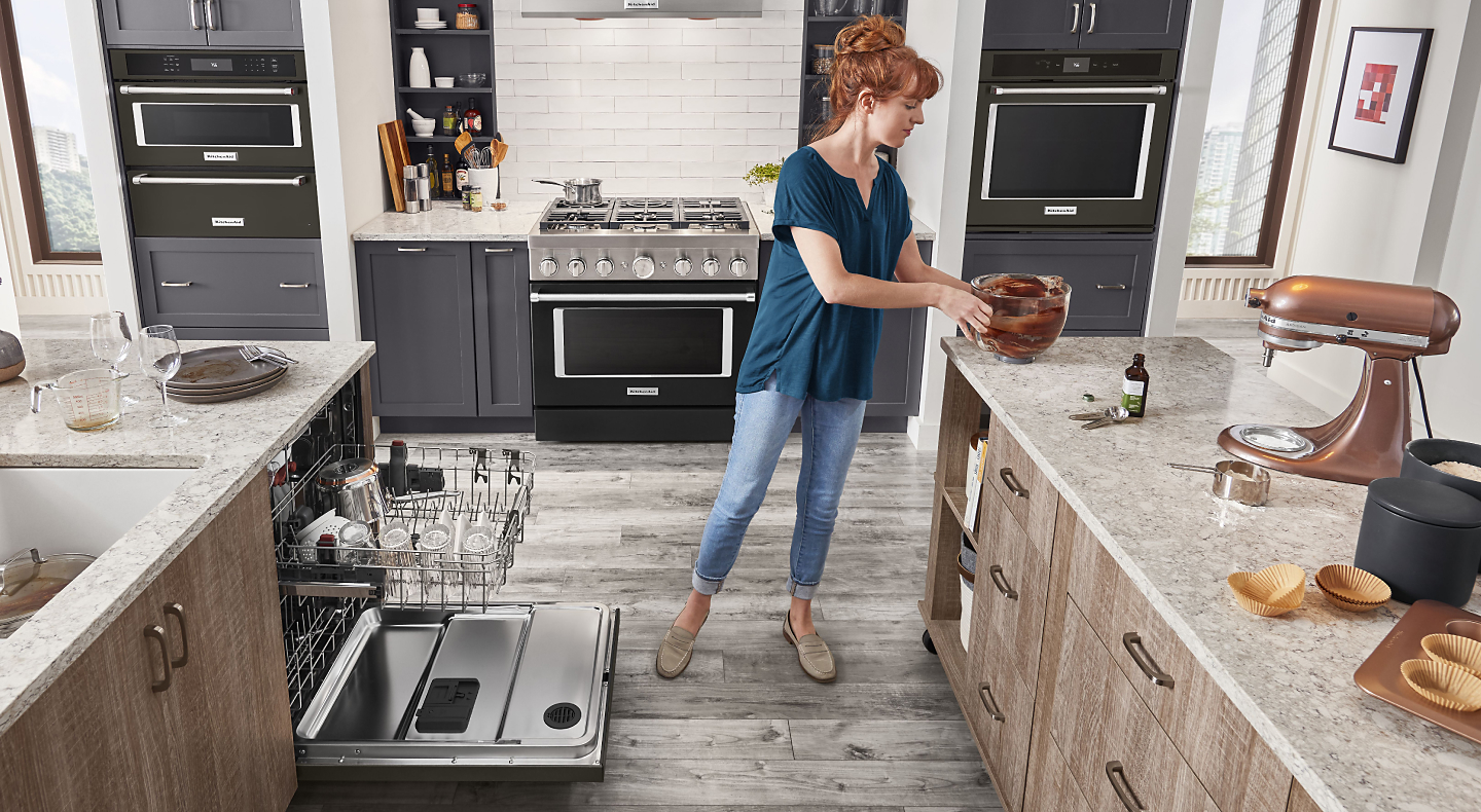 A woman placing a bowl on the counter of a modern kitchen next to a KitchenAid® dishwasher.