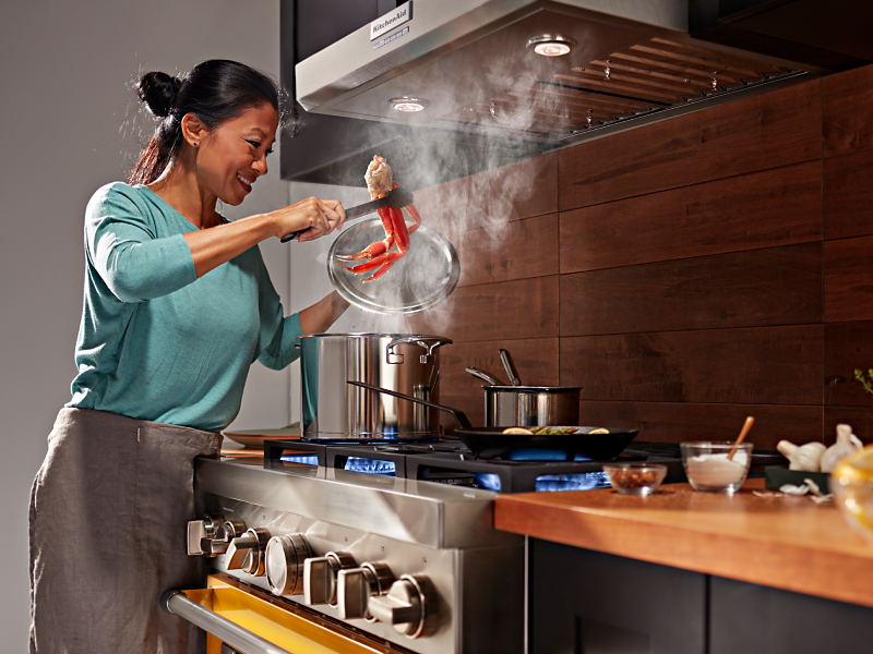 Person boiling seafood on gas burners below a range hood
