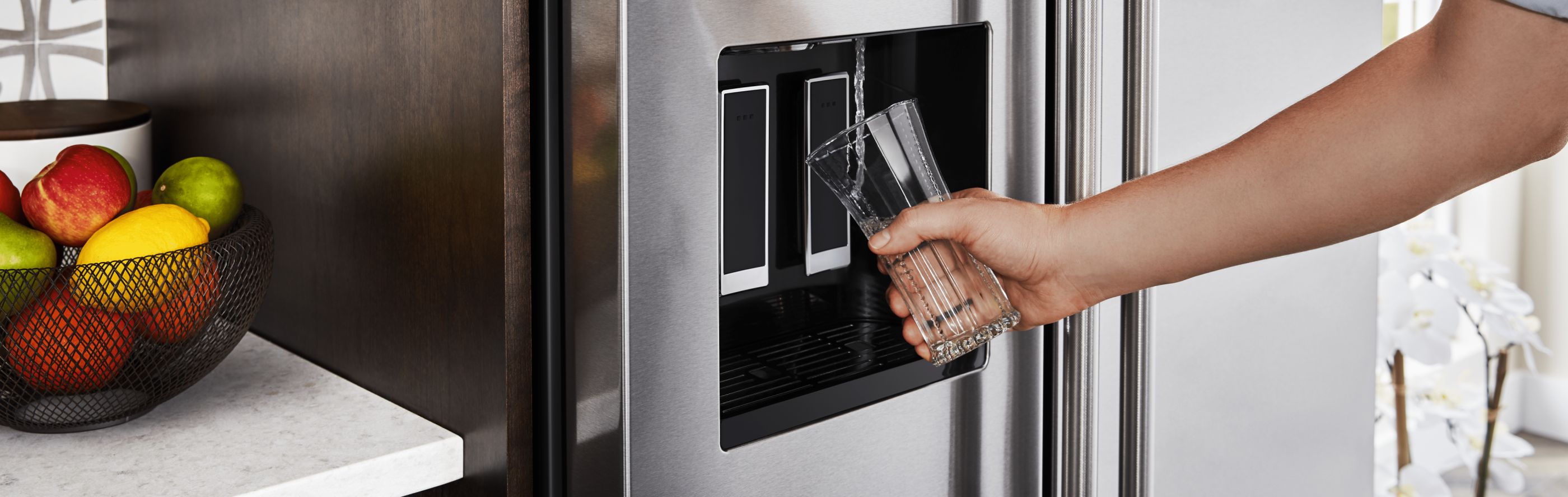 Person filling a glass of water from a refrigerator door