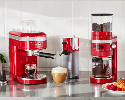 A KitchenAid® espresso machine and burr coffee grinder in a modern kitchen with an espresso, frothy cappuccino and pastry