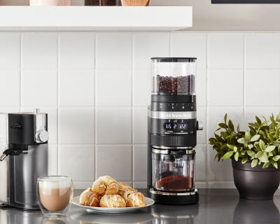 KitchenAid® burr coffee grinder next to a frothy cappuccino and pastries