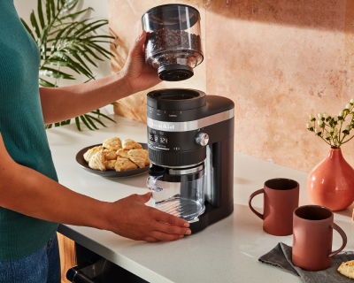 A woman using a KitchenAid® burr coffee grinder in a modern kitchen