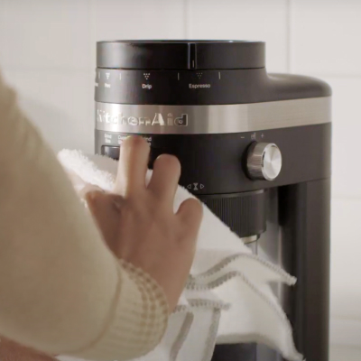Hand wiping down the exterior of a KitchenAid® Burr Grinder with a towel