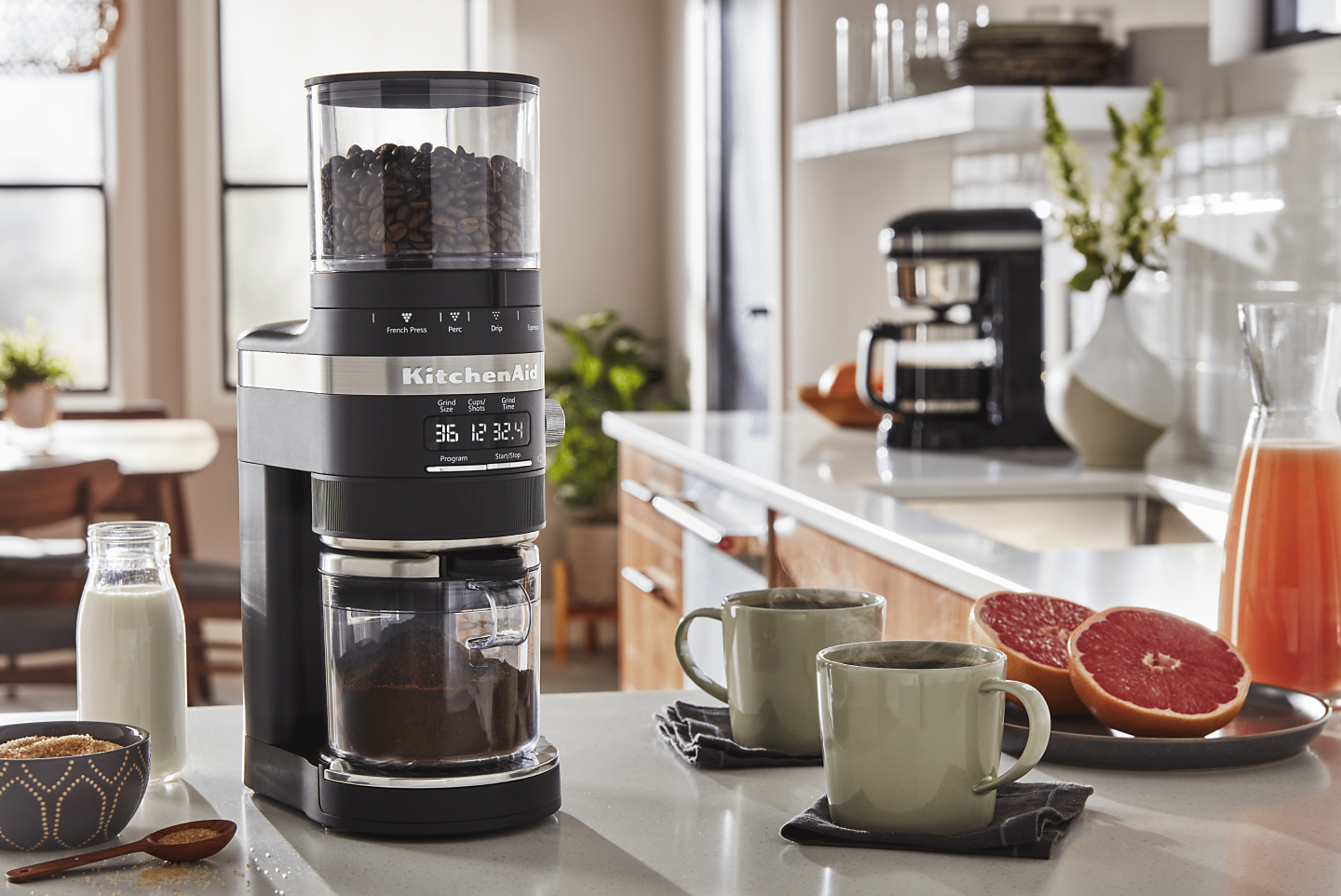 KitchenAid® burr grinder full of coffee beans next to two mugs
