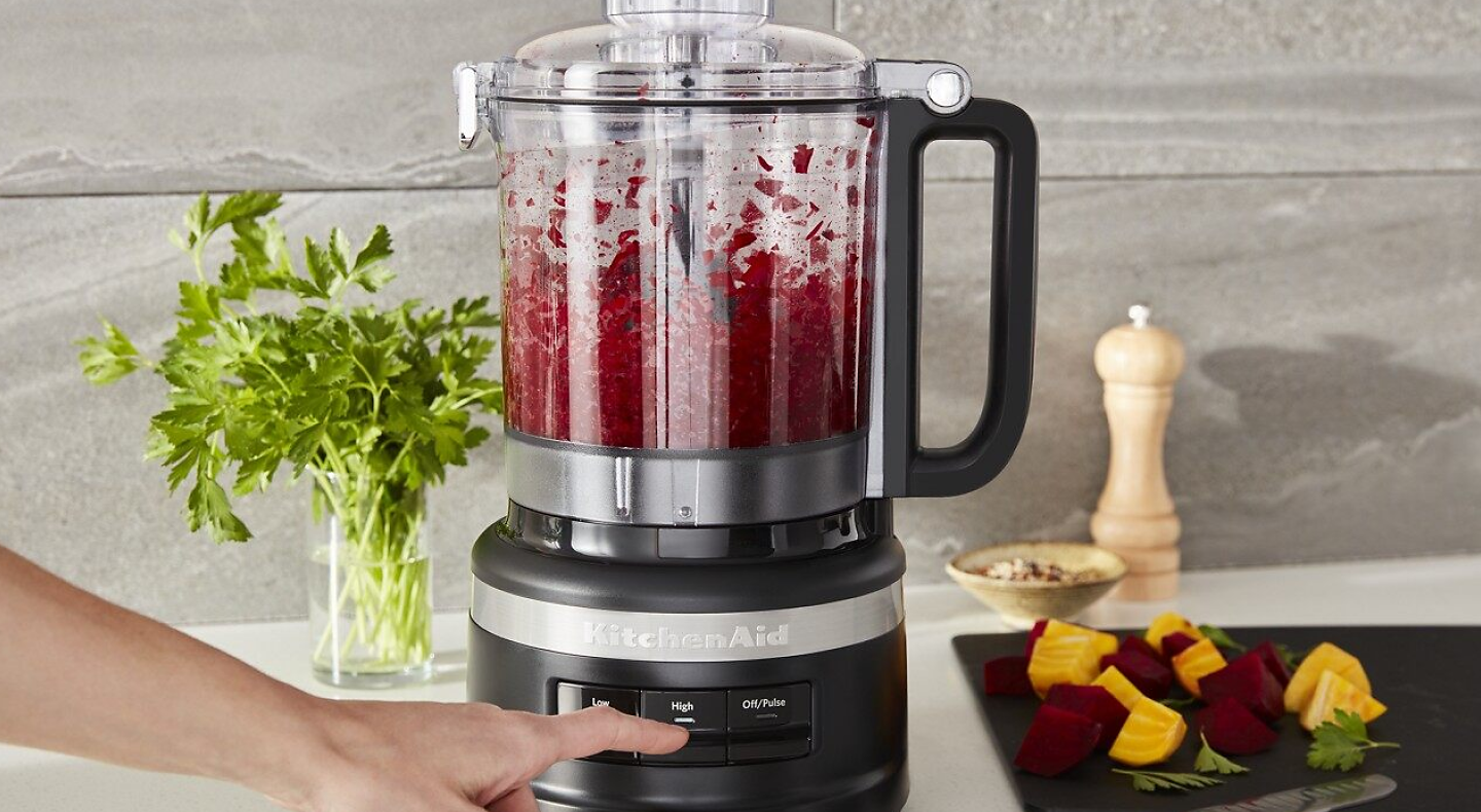 A person using a KitchenAid® food processor to process fresh ingredients