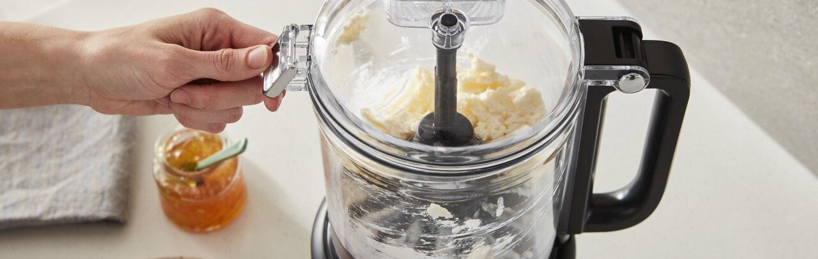 A person opening the lid of a black food processor with butter
