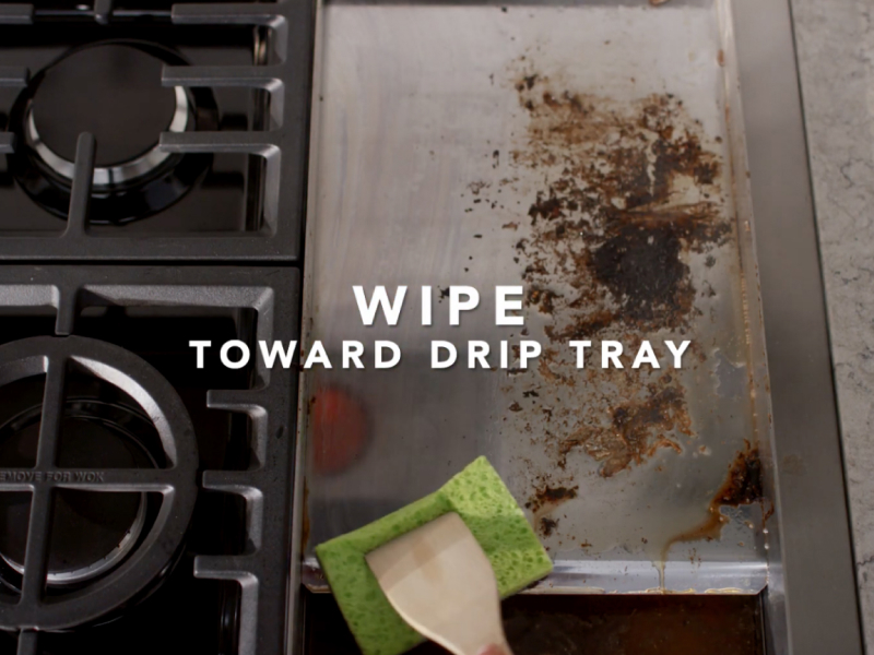 Scrubbing dirty griddle with sponge and wooden spoon
